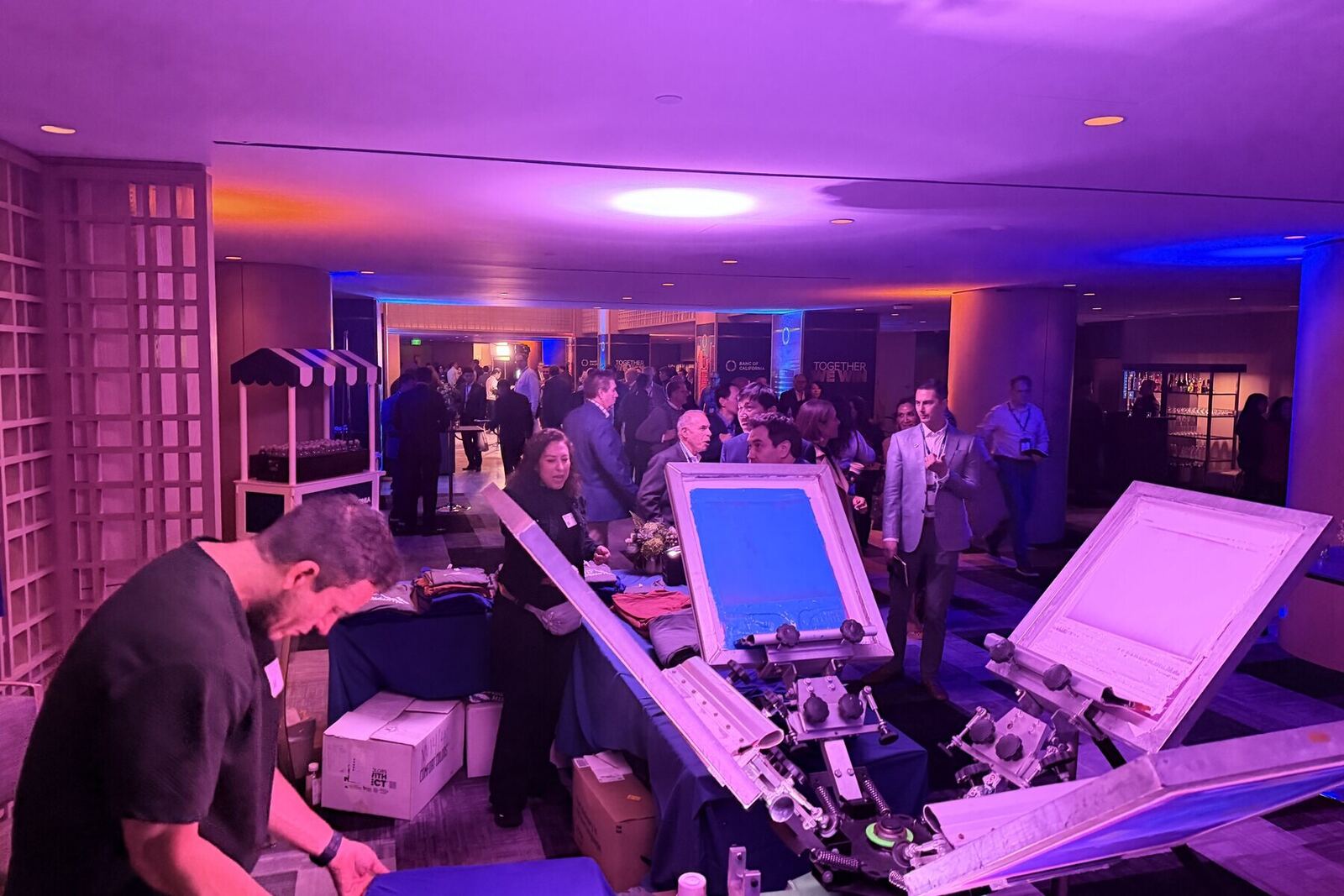 Crowd gathered at a night-lit Merch Troop brand activation printing station