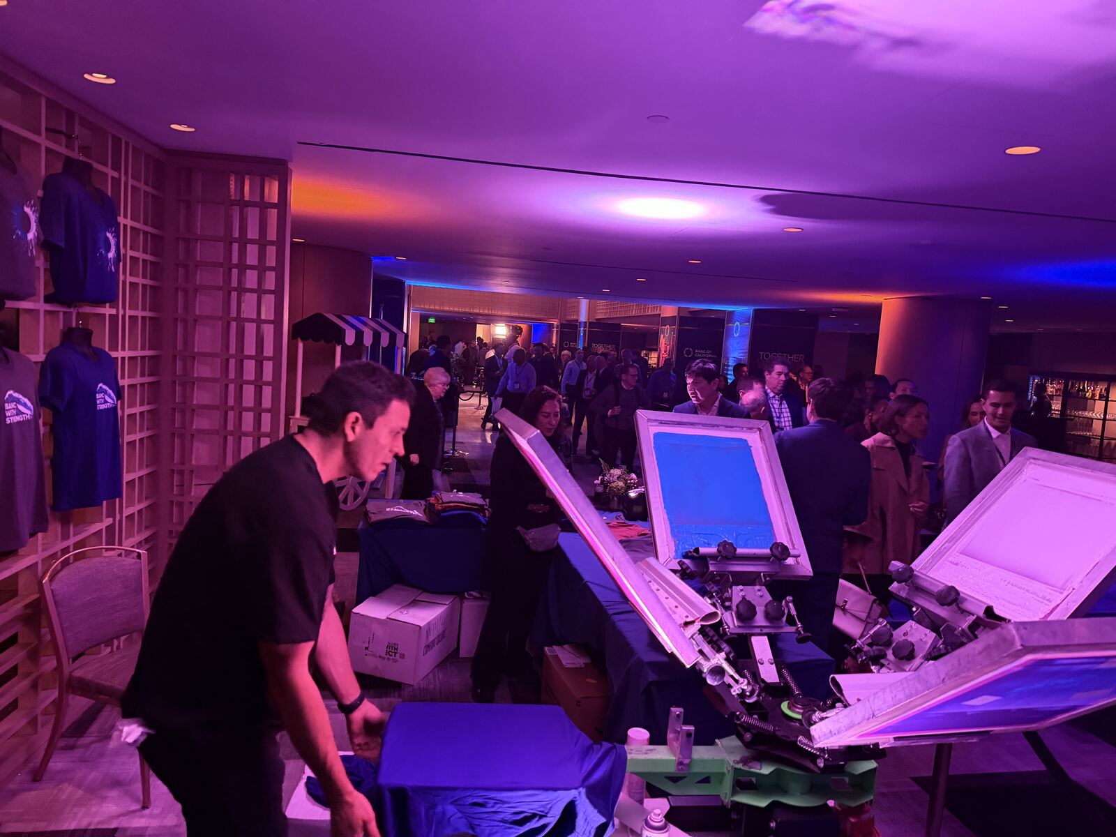 Indoor event venue with purple and blue atmospheric lighting and multiple printing demo booths